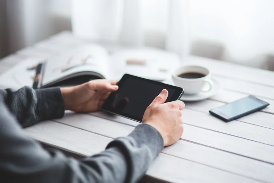 A man is using a tablet to read the news while sipping coffee, with a stylus in his hand.