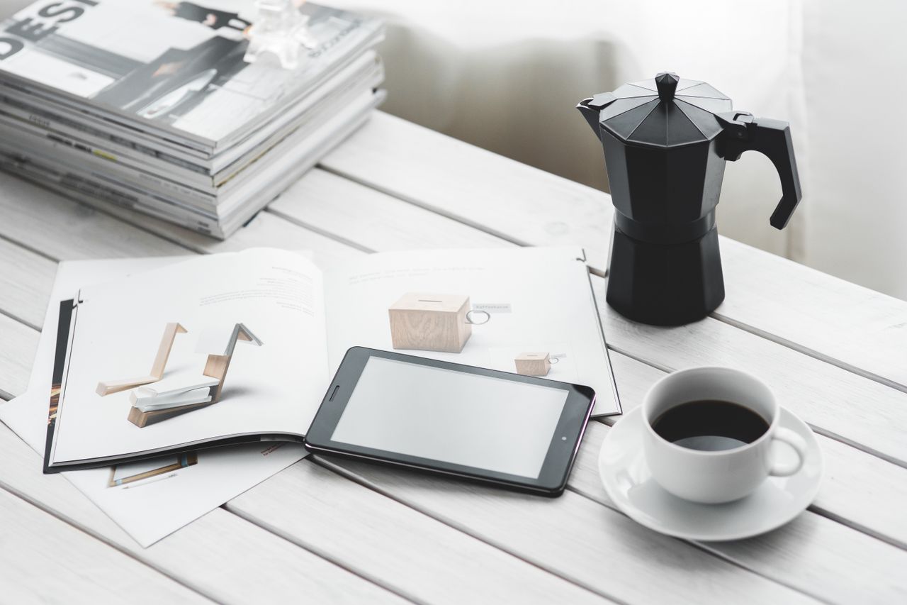 Espace de travail intérieur élégant avec une tablette, une tasse de café et des magazines posés sur une table blanche.