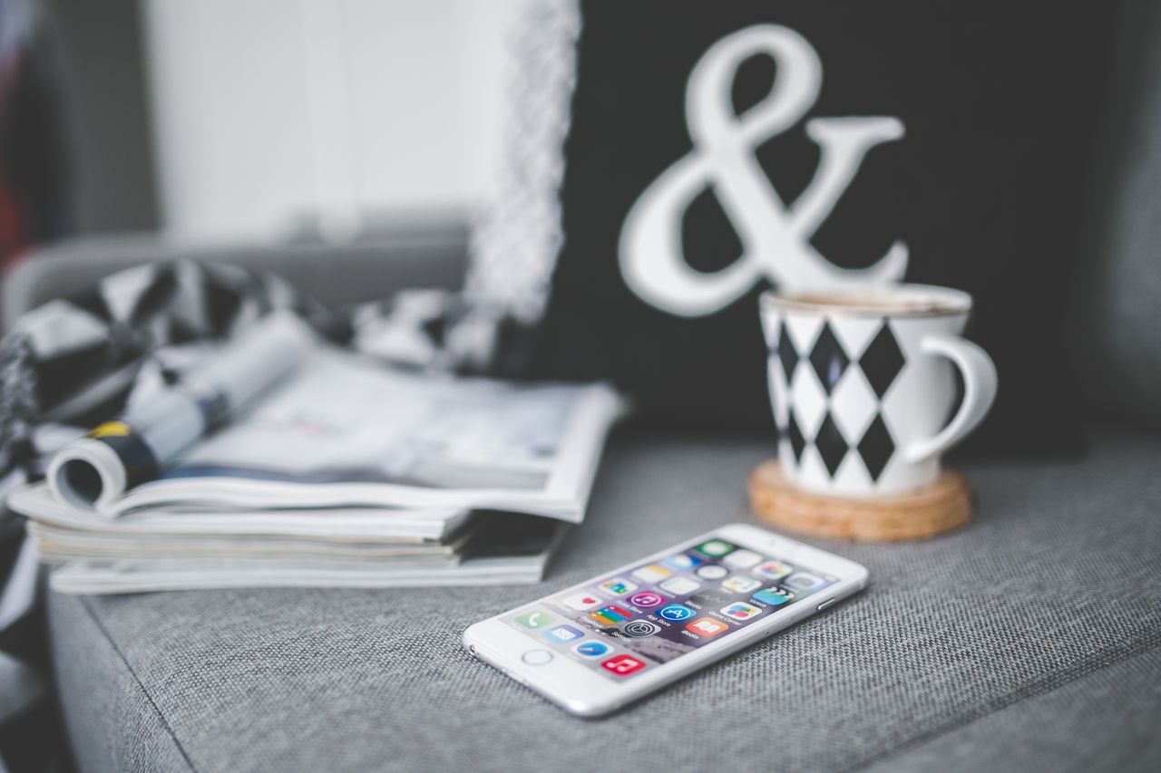 A smartphone placed beside a chic coffee cup and magazines in a comfortable couch setting.